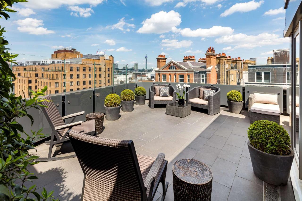 The May Fair, A Radisson Collection Hotel, Mayfair London Exterior photo The photo depicts a spacious outdoor terrace or balcony. It features modern outdoor furniture, including comfortable seating arrangements with chairs and cushions. There are several planters with neatly trimmed greenery, adding a touch of nature to t