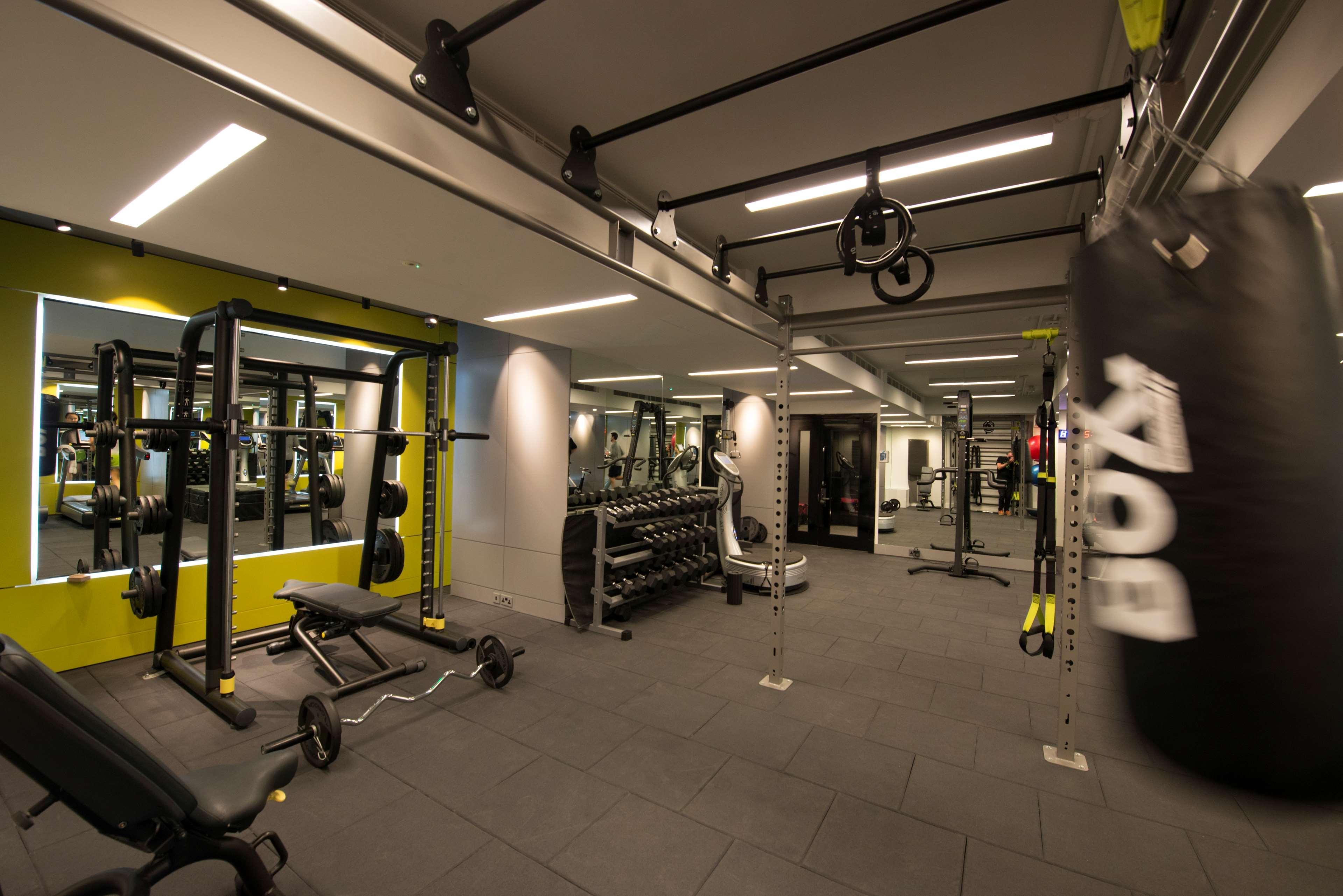 The May Fair, A Radisson Collection Hotel, Mayfair London Exterior photo The photo shows a modern gym interior. There are various fitness equipment pieces, including free weights, benches, and a multi-functional weight rack. The lighting is bright, with a mix of ceiling lights and mirrors on the walls that enhance the spa