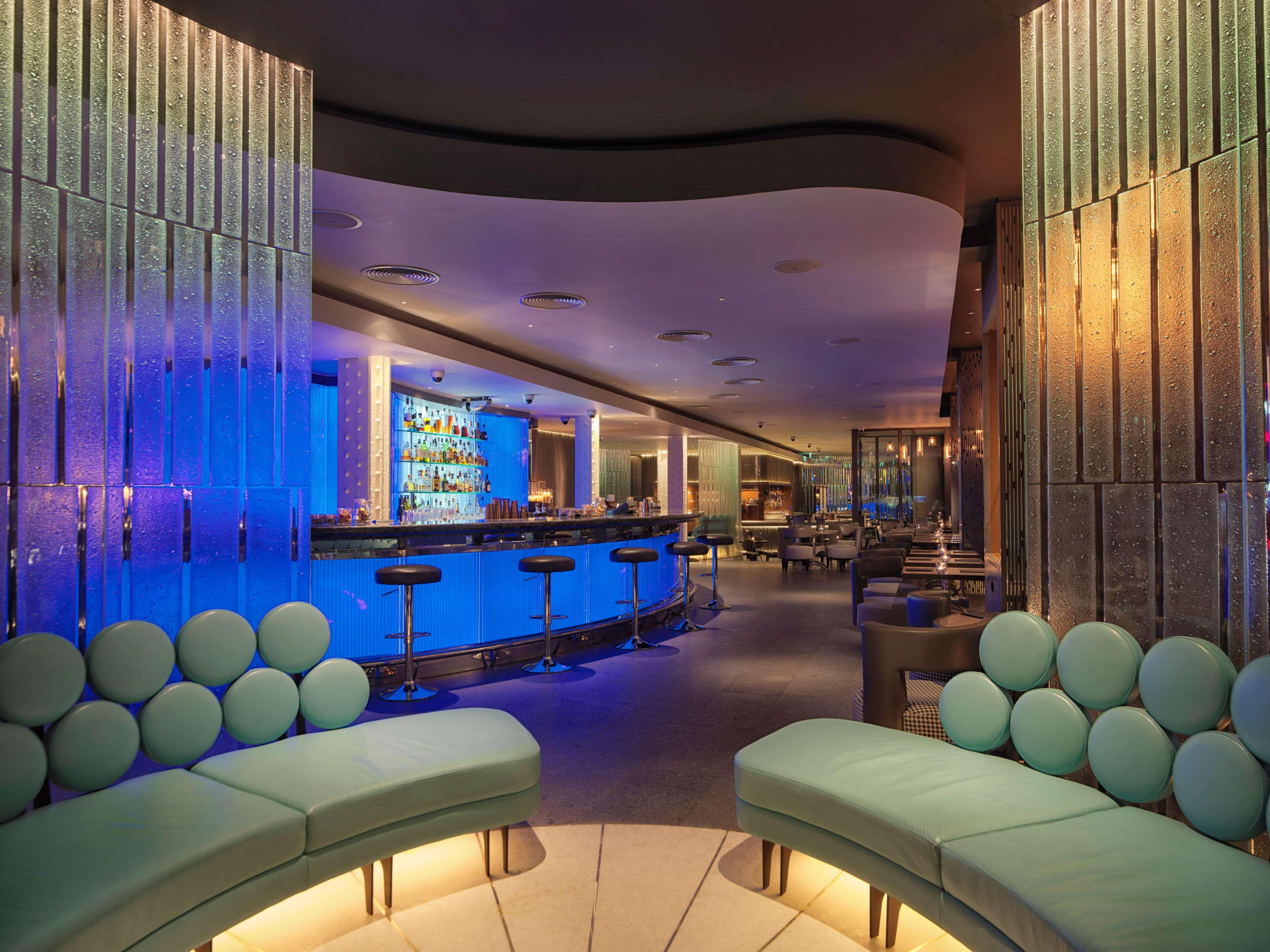 The May Fair, A Radisson Collection Hotel, Mayfair London Exterior photo The photo shows a modern bar or lounge area with a stylish and contemporary design. The interior features curved seating with light green upholstery, creating a relaxed atmosphere. Behind the seating, there is a bar area illuminated with blue lightin