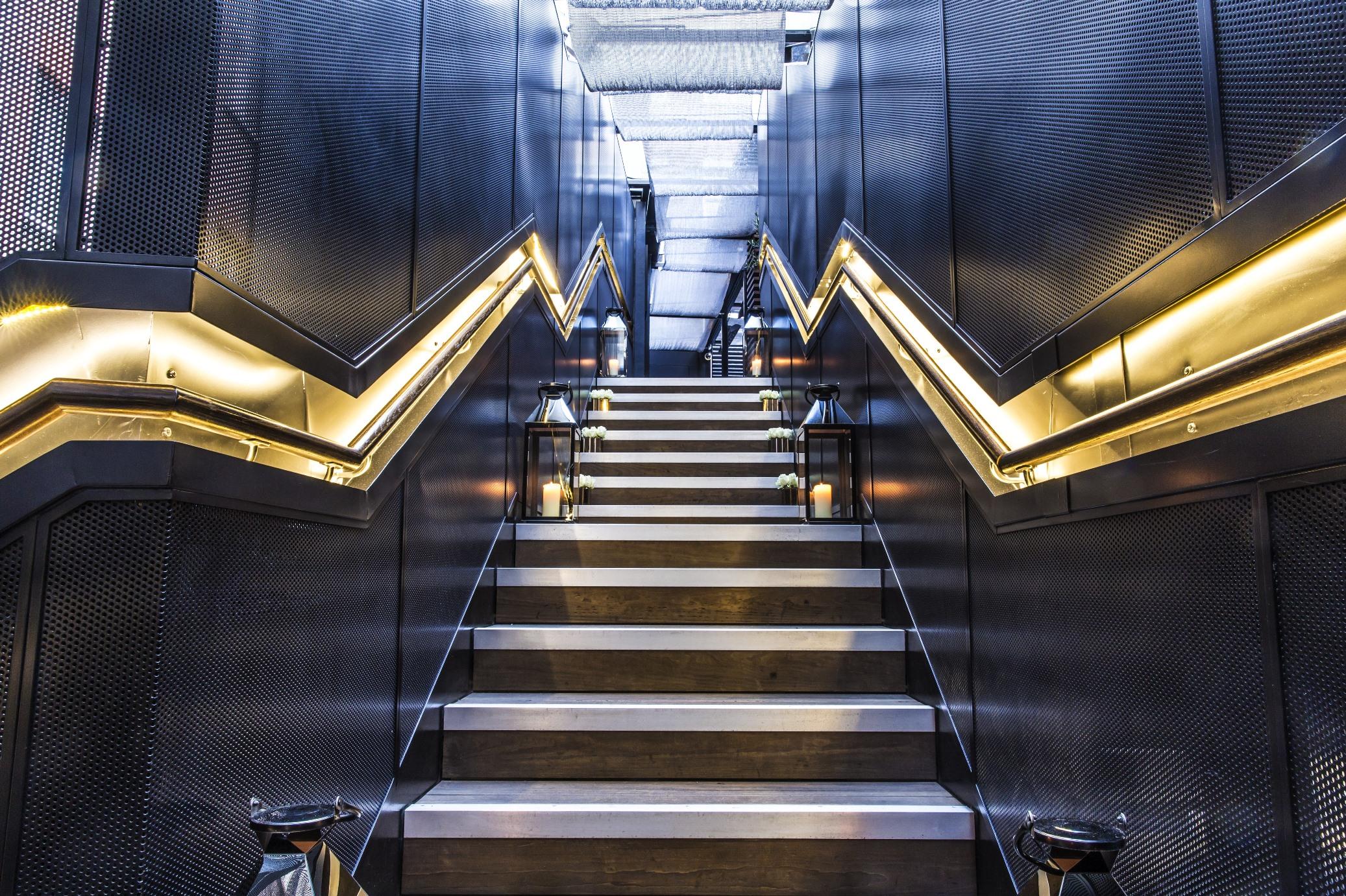 The May Fair, A Radisson Collection Hotel, Mayfair London Exterior photo The photo depicts a staircase with a modern and sleek design. The steps are a combination of metal and wood, creating a stylish contrast. The walls on either side of the staircase are characterized by a textured, dark material, with zigzag-shaped lig