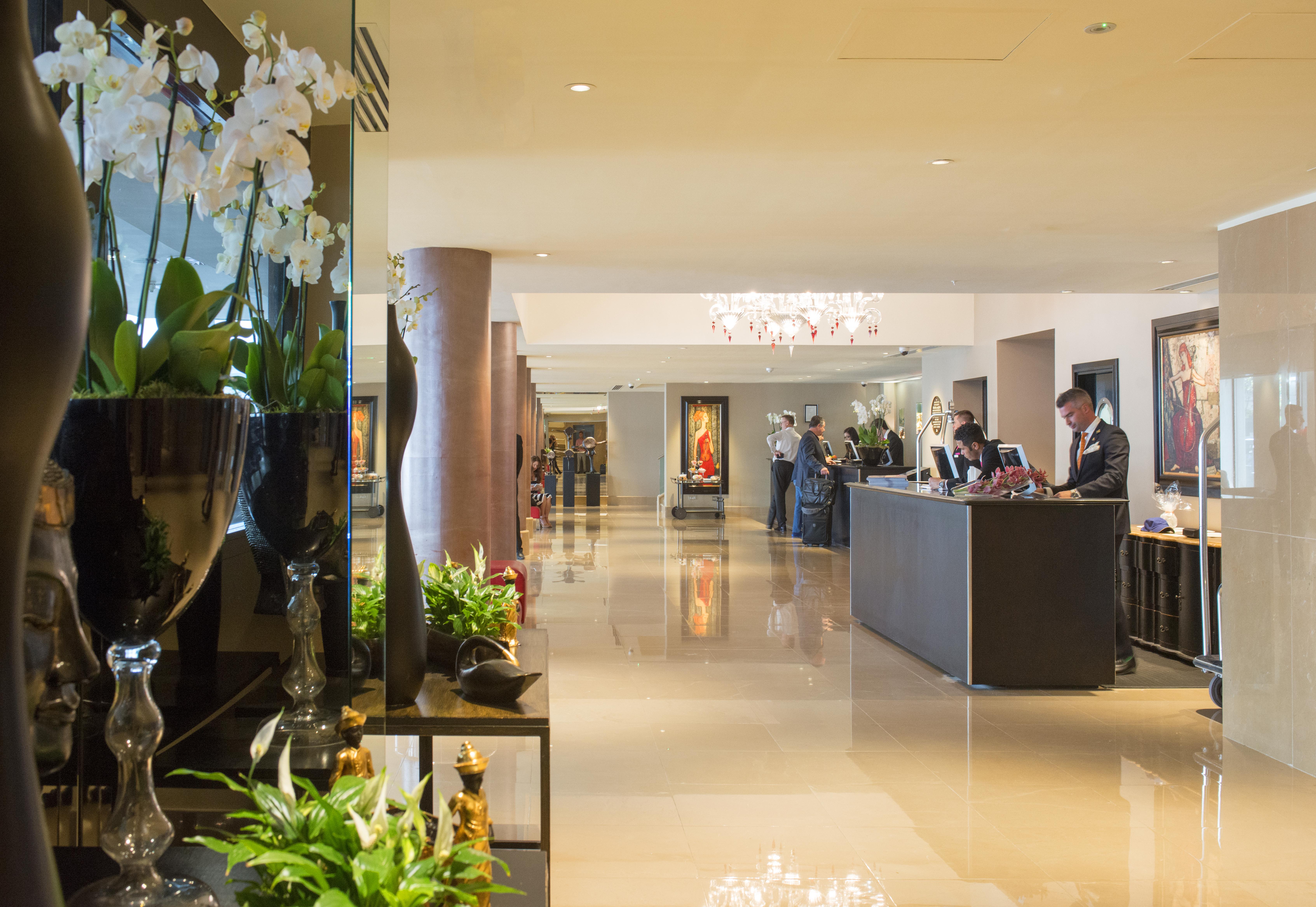 The May Fair, A Radisson Collection Hotel, Mayfair London Exterior photo The photo shows a spacious and elegantly designed hotel lobby. There are decorative elements such as flowers and plants along the sides, enhancing the luxurious atmosphere. In the background, you can see the reception area with staff members engaged 